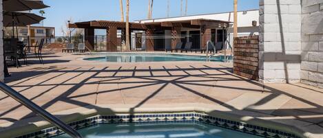 A pool area with a tiled edge, lounge chairs, and a covered seating area.