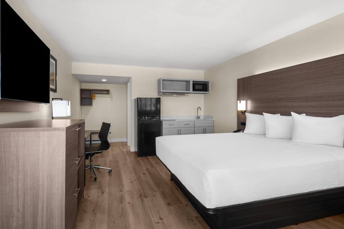 A hotel room with a bed, a desk, a chair, a refrigerator, a microwave, and a television.