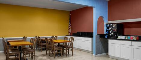 Un restaurante con una pared amarilla, una pared roja y un techo azul. Hay mesas y sillas de madera, y se ve una bandera estadounidense.