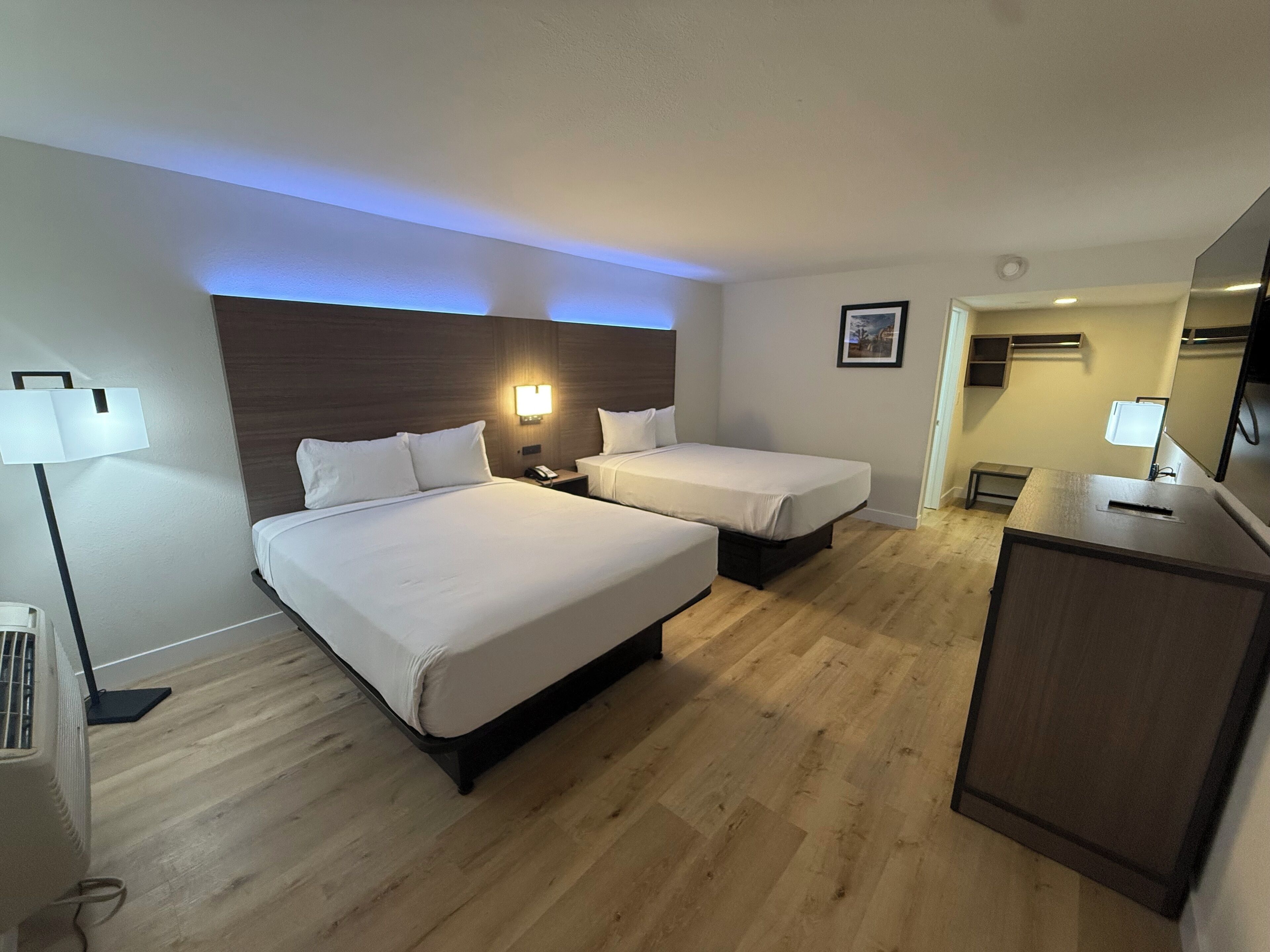 A hotel room with two beds, a desk, a lamp, and a picture on the wall.