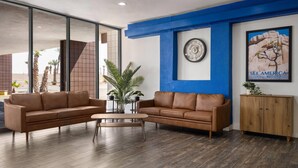 A modern lobby with two leather sofas, a wooden coffee table, a large framed clock, a poster of a desert landscape, and a wooden cabinet. - Travelodge by Wyndham Imperial/El Centro (Imperial)