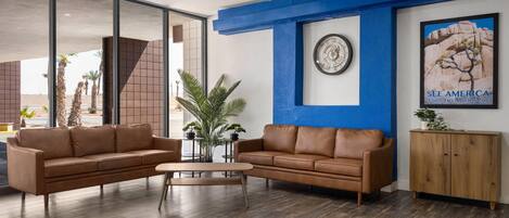 A modern lobby with two leather sofas, a wooden coffee table, a large framed clock, a poster of a desert landscape, and a wooden cabinet.