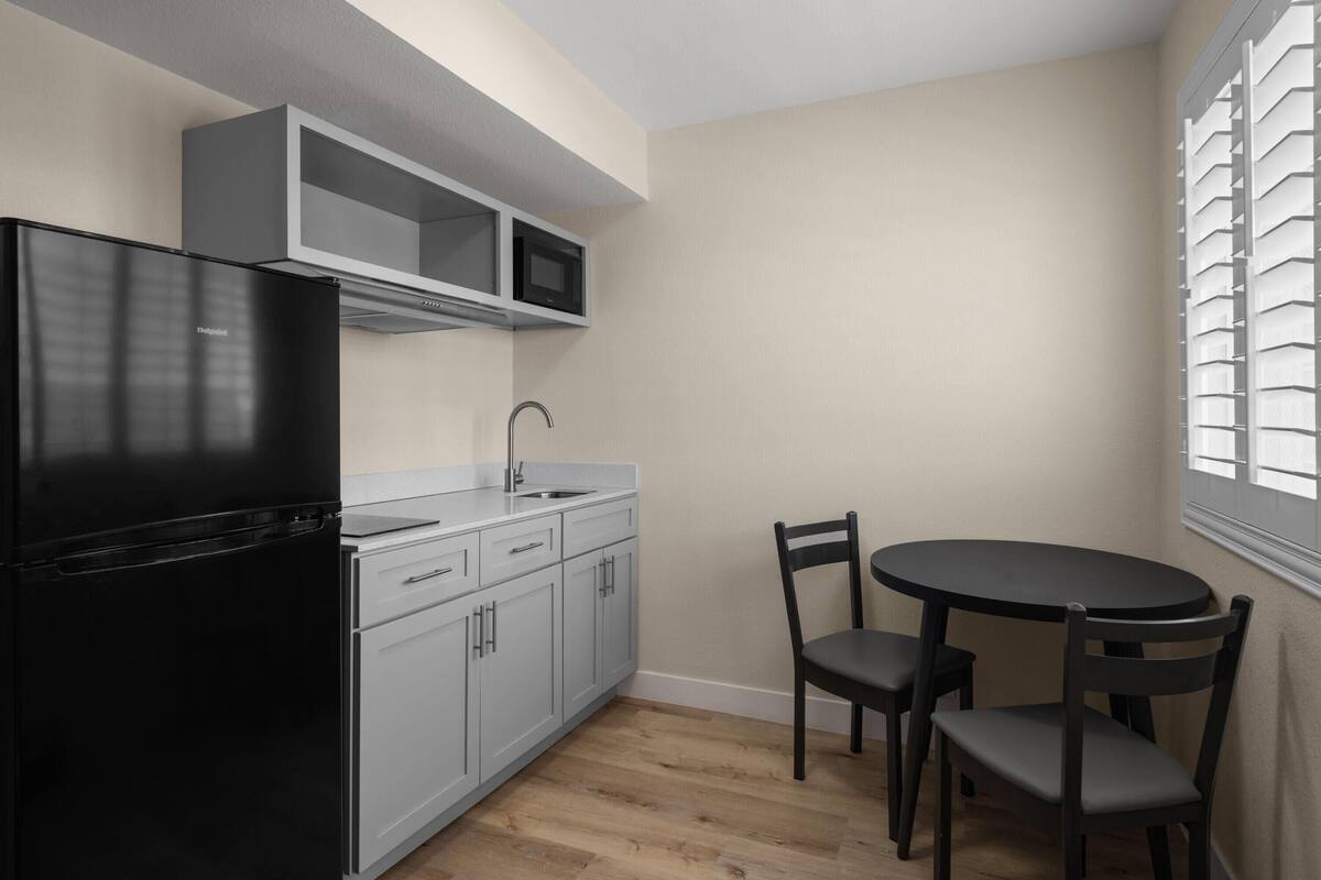 A compact kitchen with a black refrigerator, a microwave, and a sink. There is a dining table with two chairs.