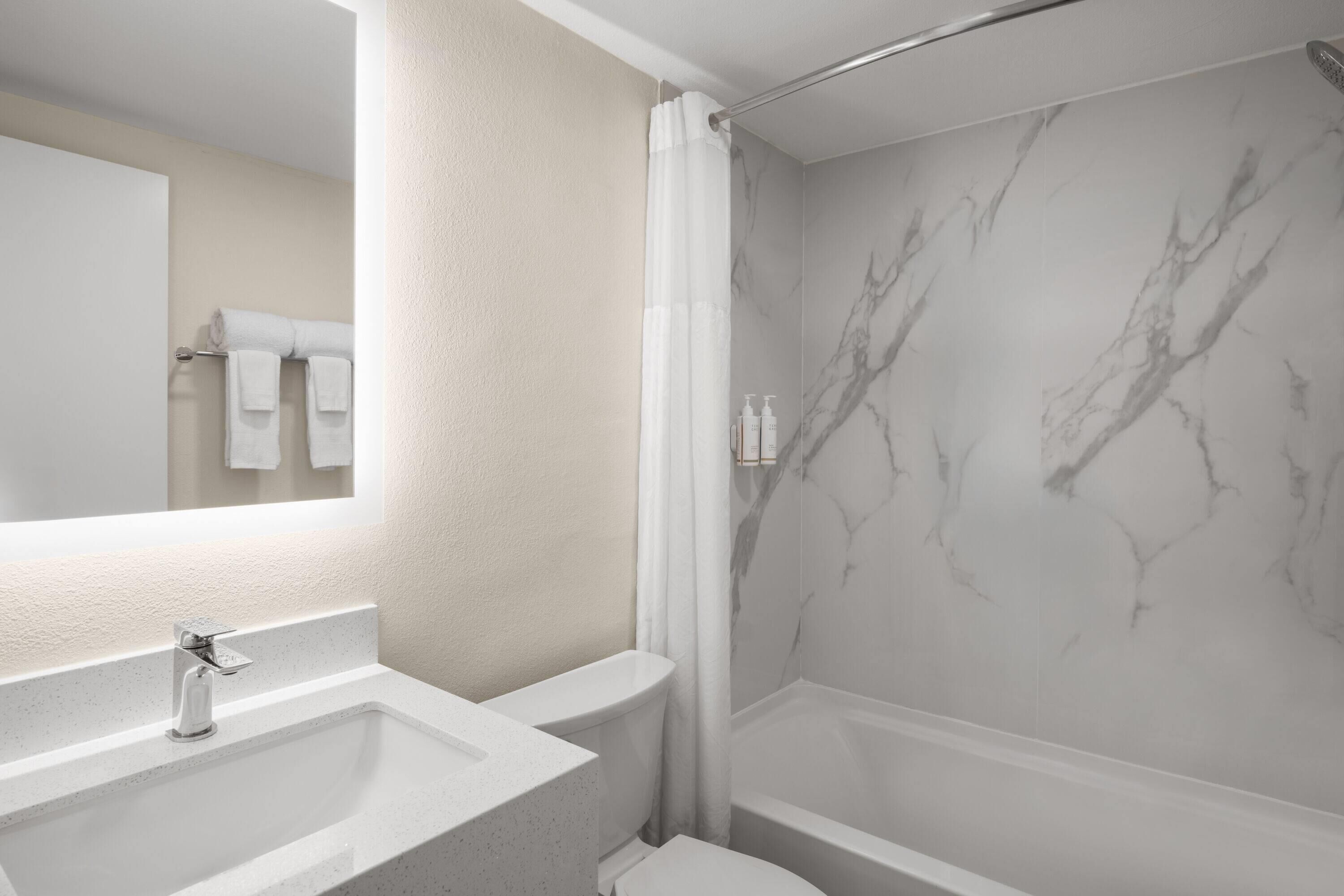 Un baño con pared de ducha de mármol, lavamanos y retrete.