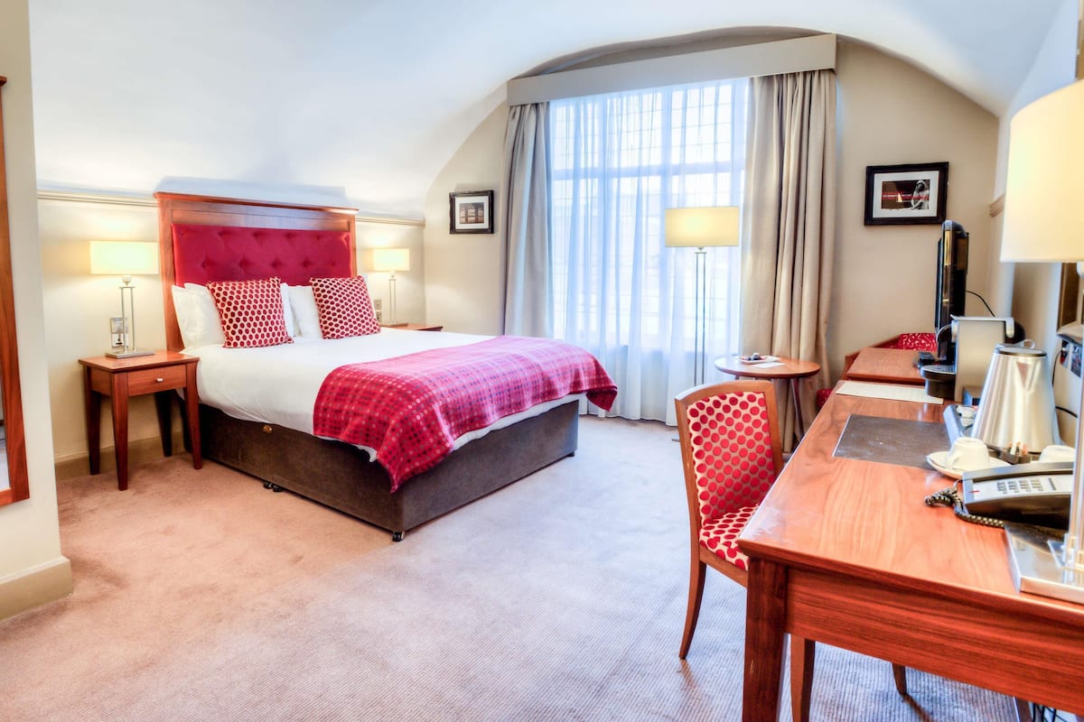 A hotel room with a large bed, a desk, a chair, a TV, and a window with curtains.