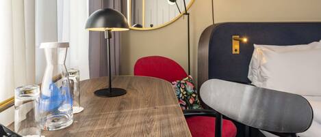 Una habitación de hotel con una mesa de madera, un escritorio con una computadora, una cama con cabecera y un espejo en la pared.