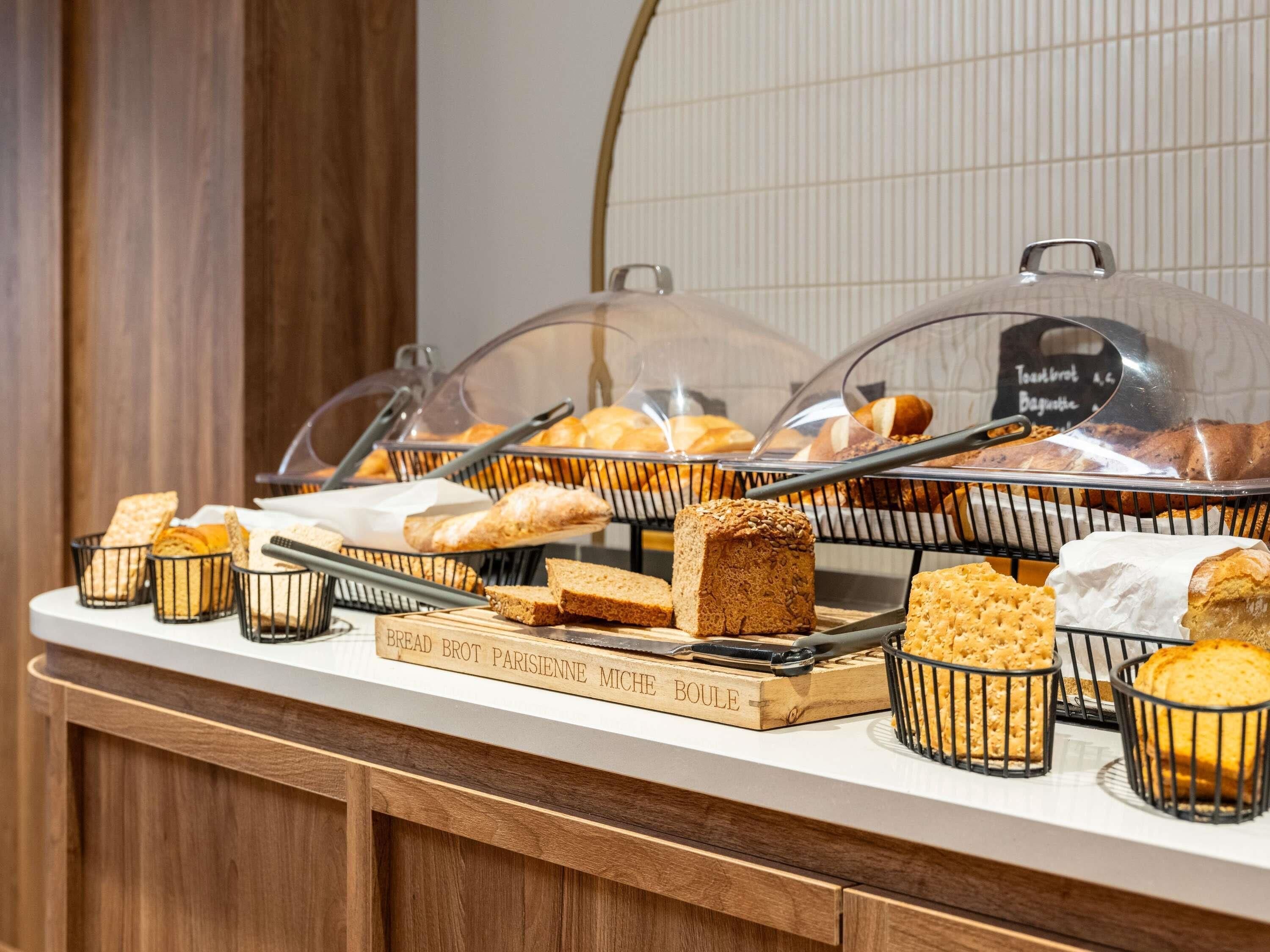 A buffet with various breads and pastries displayed in baskets and under glass covers.