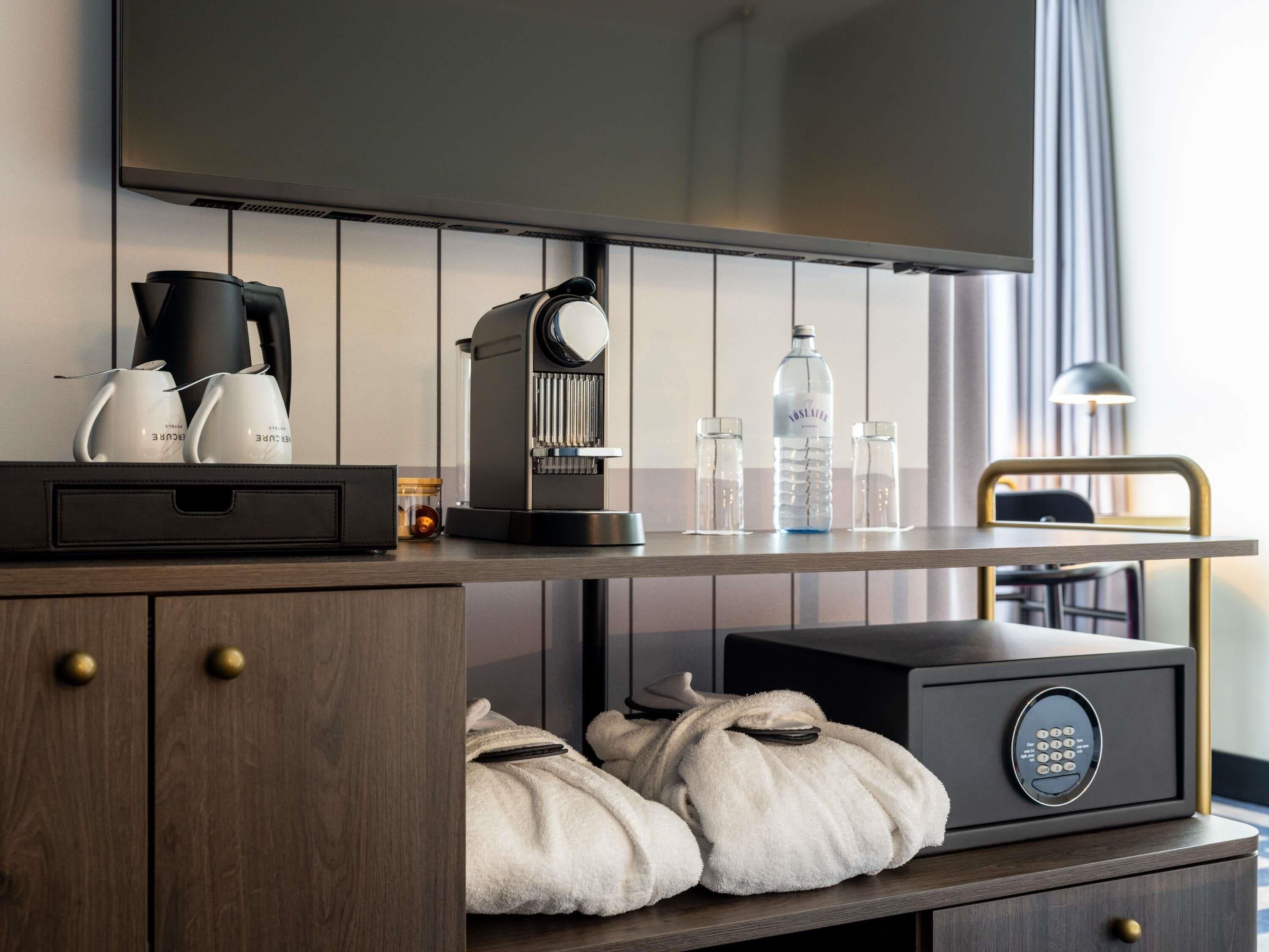 A modern hotel room with a flat-screen TV, a coffee machine, a water dispenser, and a safe.