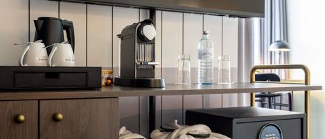 A modern hotel room with a flat-screen TV, a coffee machine, a water dispenser, and a safe.