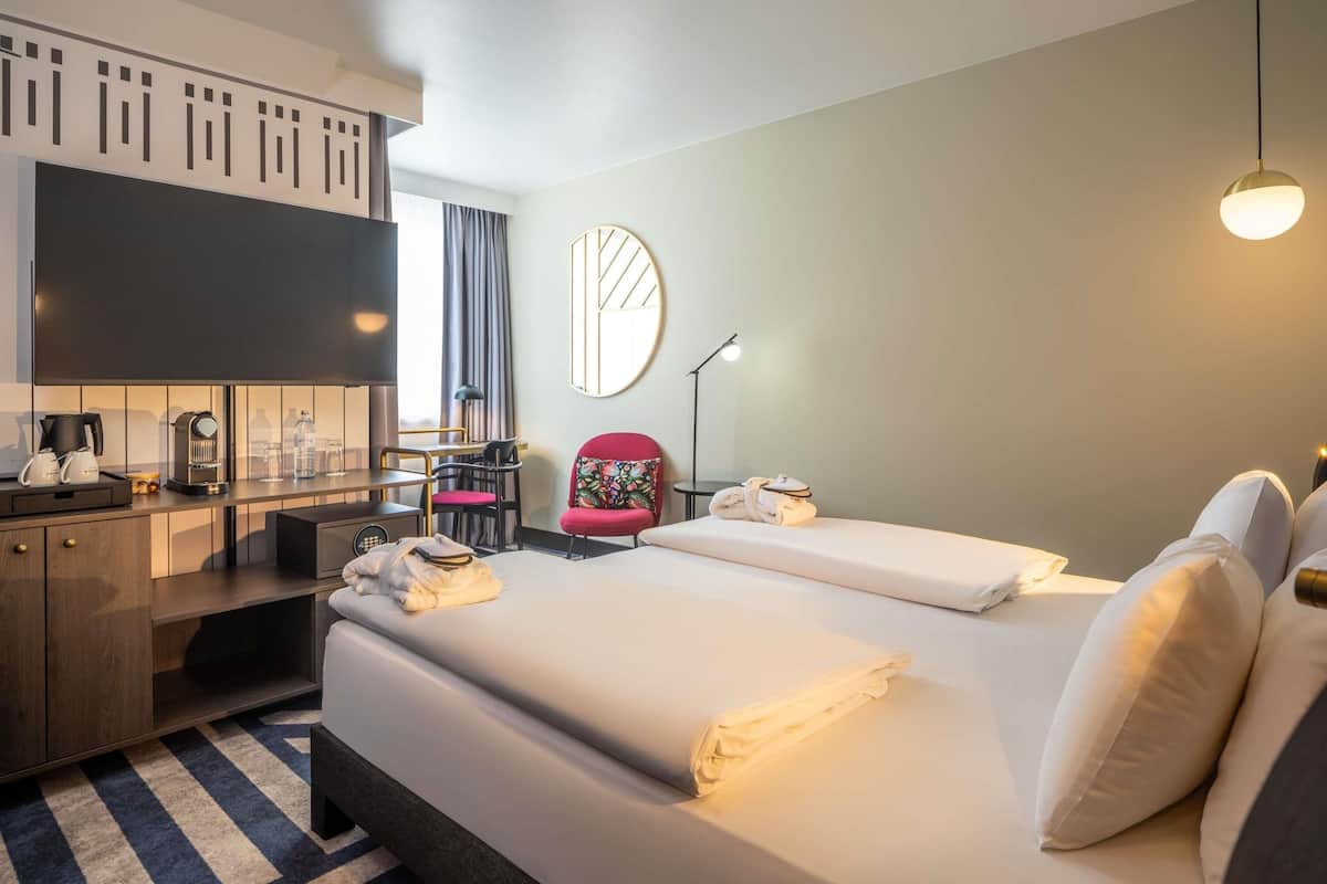 Quarto de hotel com cama, escrivaninha, cadeira, espelho e luminária.