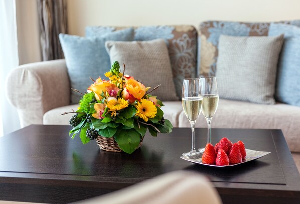 A dining table with a floral arrangement, two glasses of white wine, and a plate of strawberries.