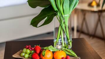 Una presentación ordenada de frutas y flores sobre una mesa en una habitación de hotel, con una cama y una lámpara al fondo.