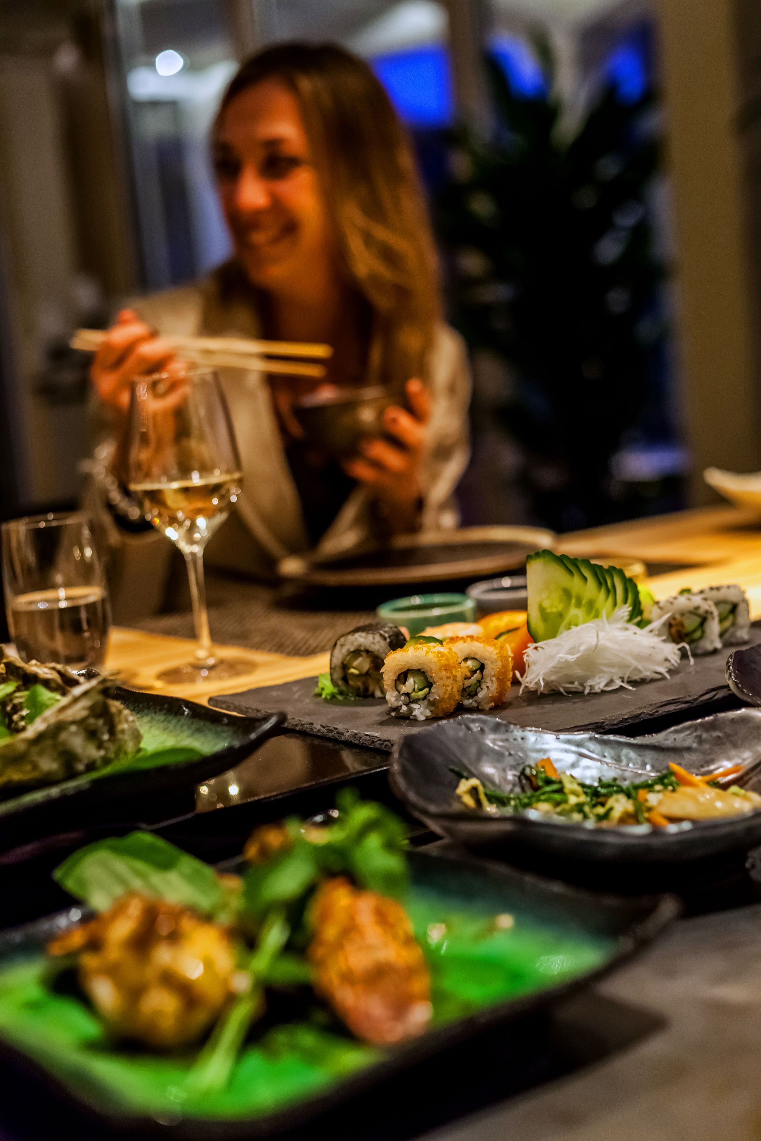 Una mesa de comedor con diversos platos, incluyendo sushi y una copa de vino.