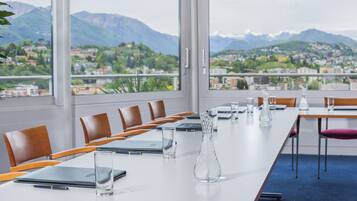 Une salle de conférence avec une longue table, des chaises et une vue sur les montagnes et une ville.