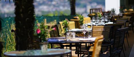 An outdoor dining area with tables and chairs, palm trees, and a view of the landscape.