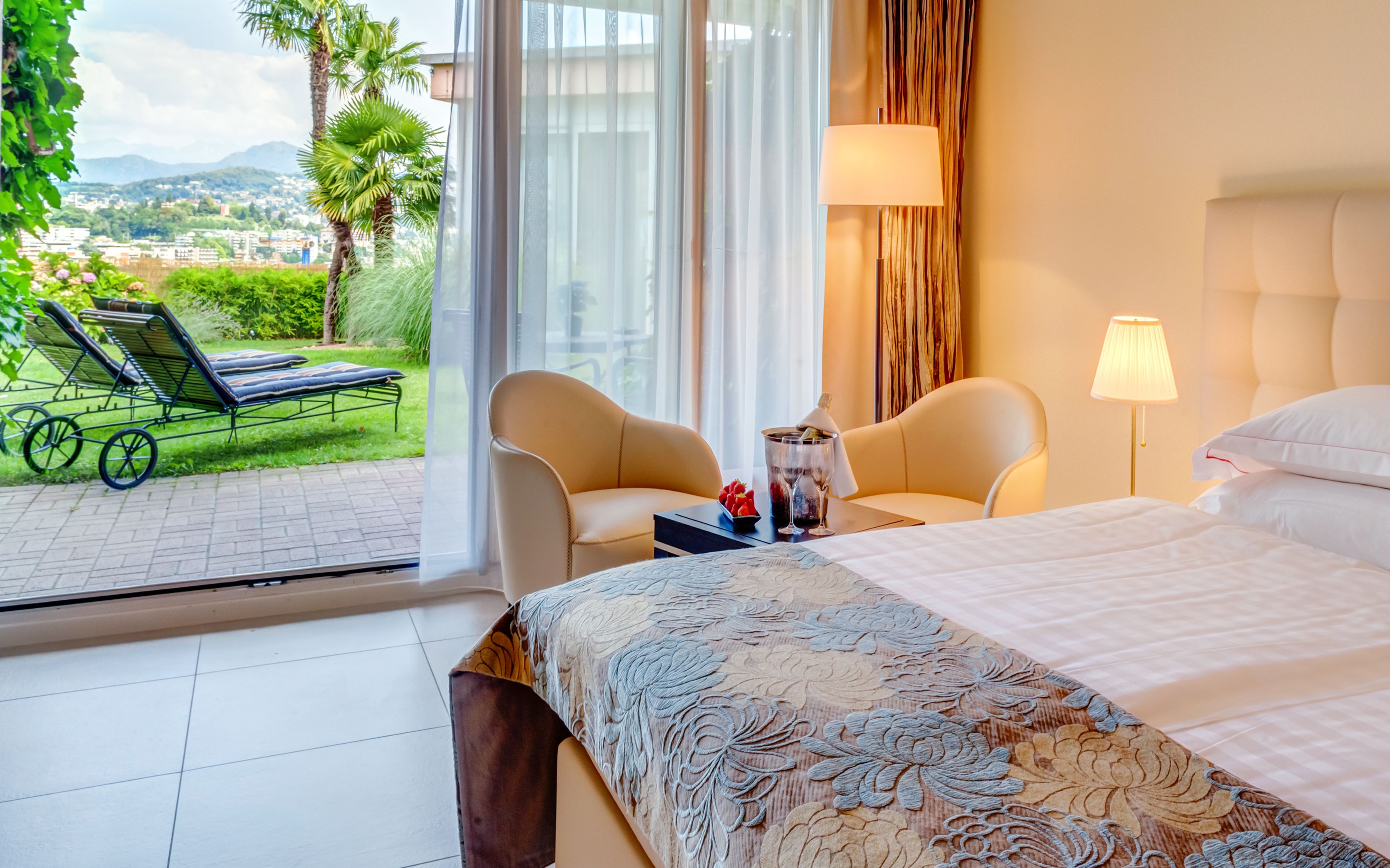 Una habitación de hotel con cama, dos sillas, una mesa con una bebida y vista al exterior.