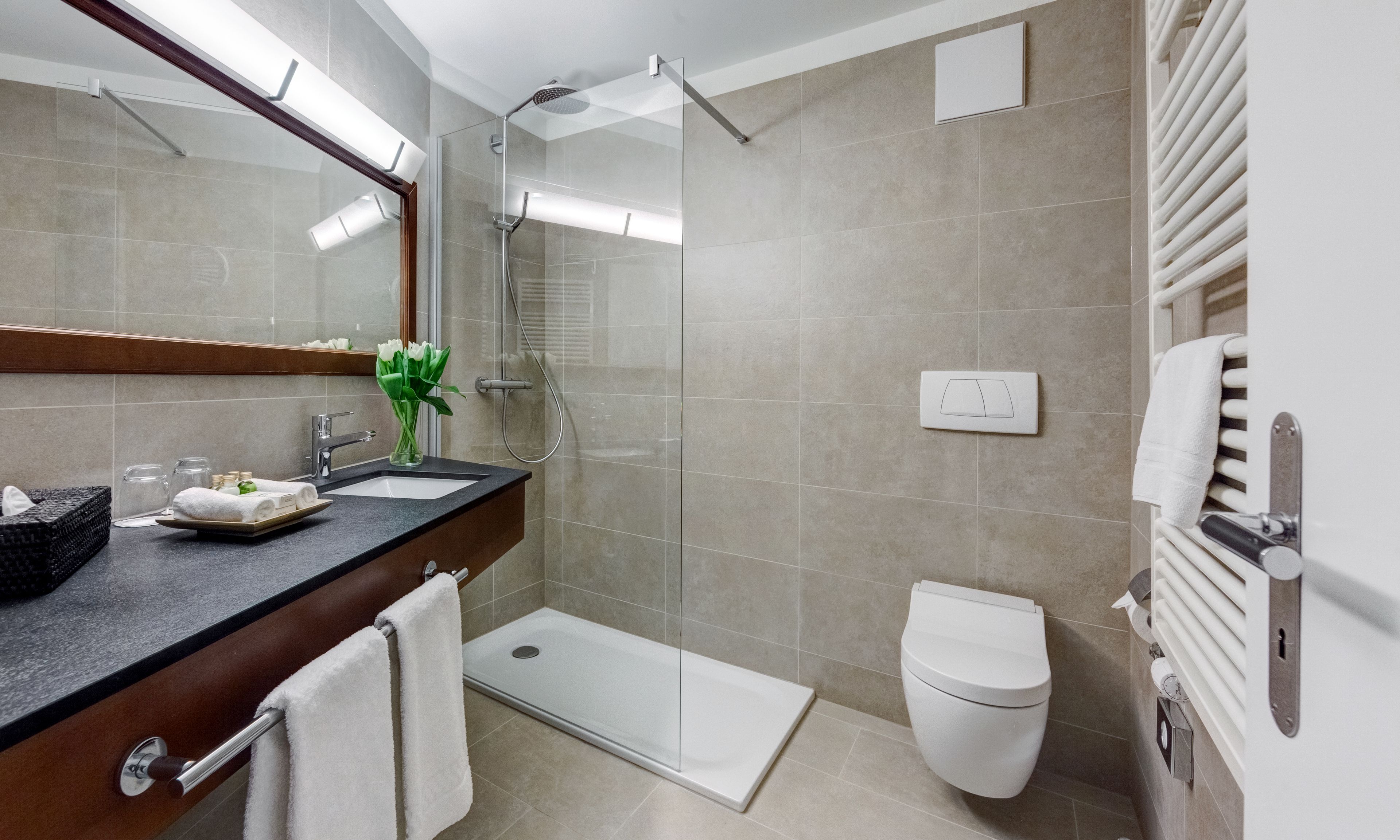 Un baño moderno con cabina de ducha de vidrio, inodoro blanco y tocador con espejo y lavamanos.