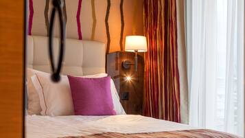 A hotel room with a bed, a nightstand, a lamp, and a view of the outside.