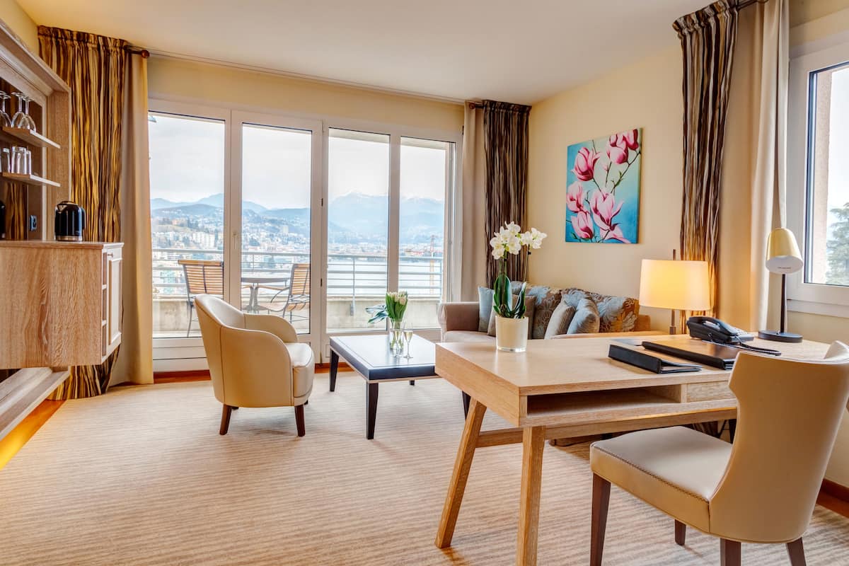 Habitación de hotel con comedor, sofá, mesa de centro y vistas a la ciudad y las montañas.