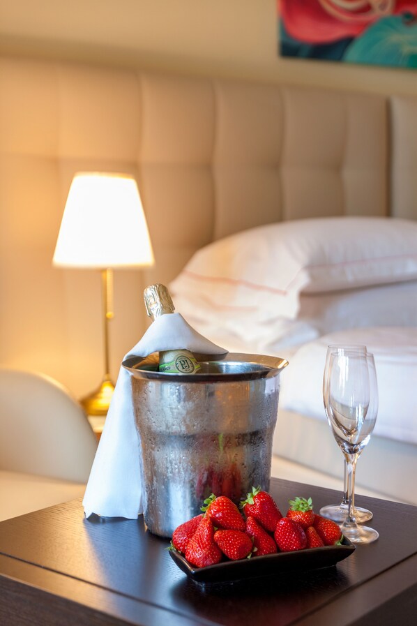 A bed with white linens, a bedside lamp, a bucket with a bottle of champagne, a glass, and a plate of strawberries on a wooden nightstand.