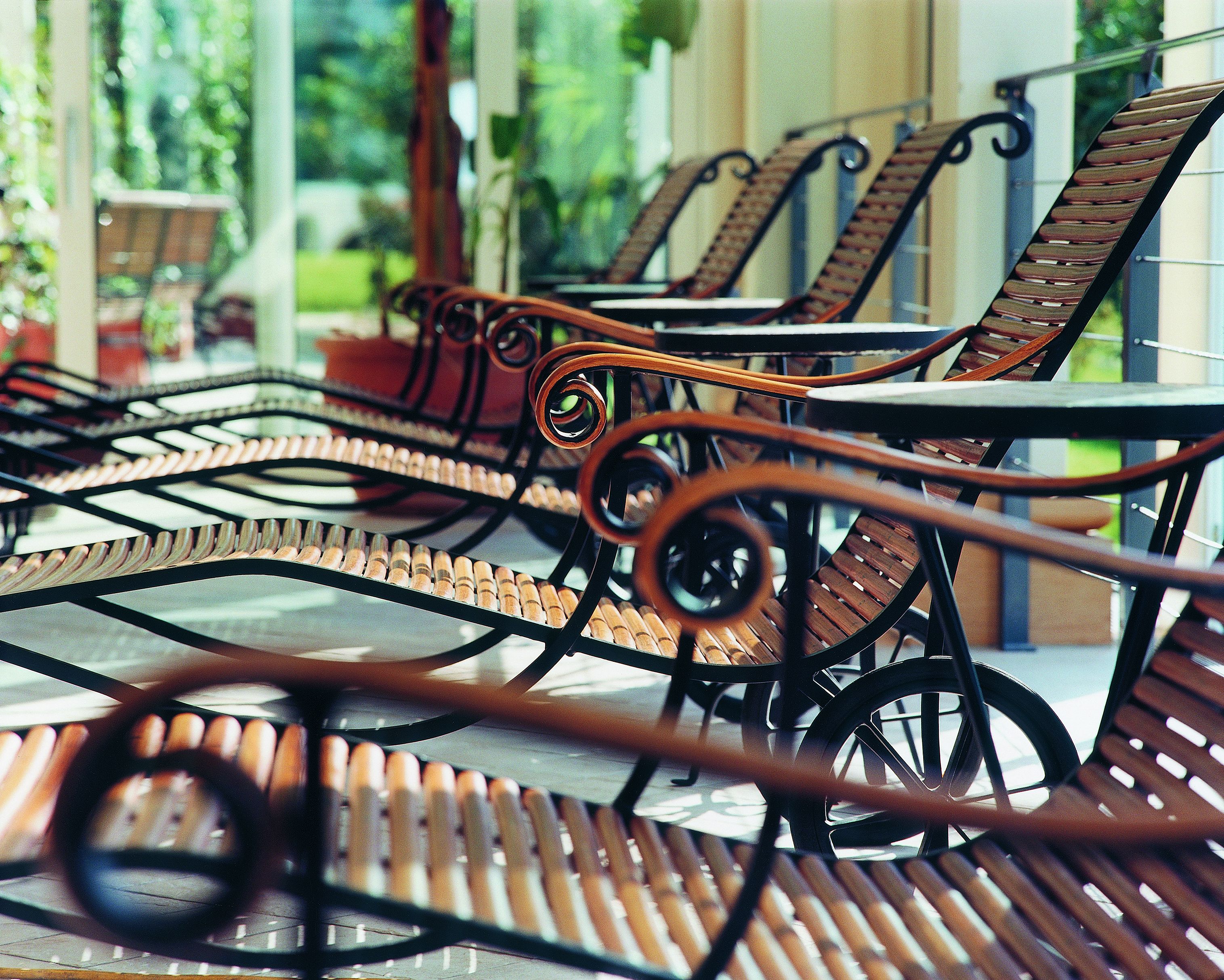 A row of outdoor metal chairs with intricate designs, arranged on a patio with a view of greenery in the background.