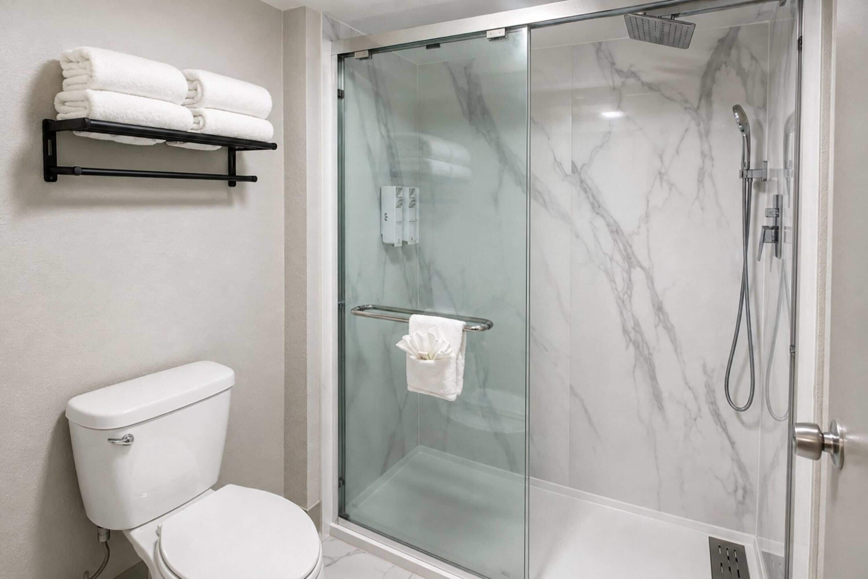 A modern bathroom with a glass-enclosed shower, a toilet, and a towel rack with folded towels.