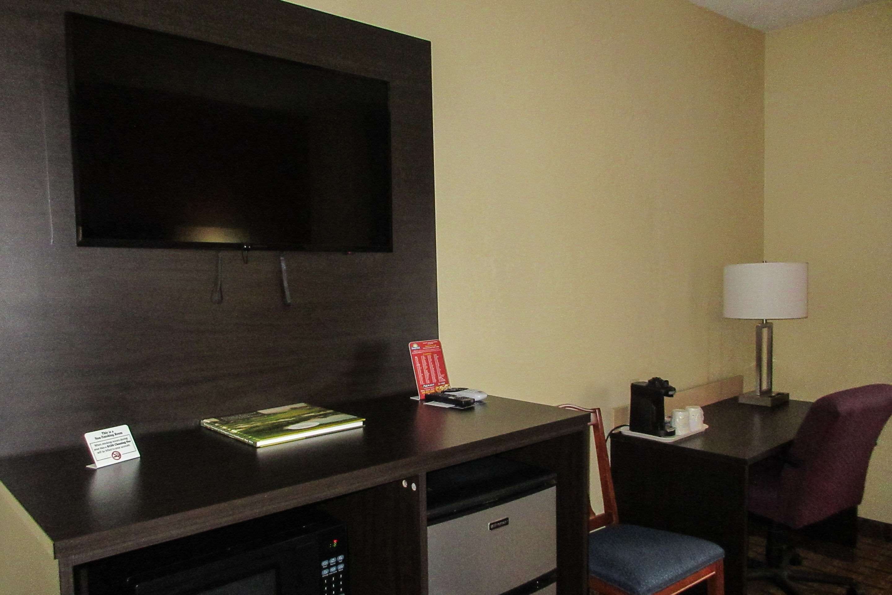A hotel room with a dark wooden desk, a flat-screen TV, a lamp, a chair, and a small coffee maker.