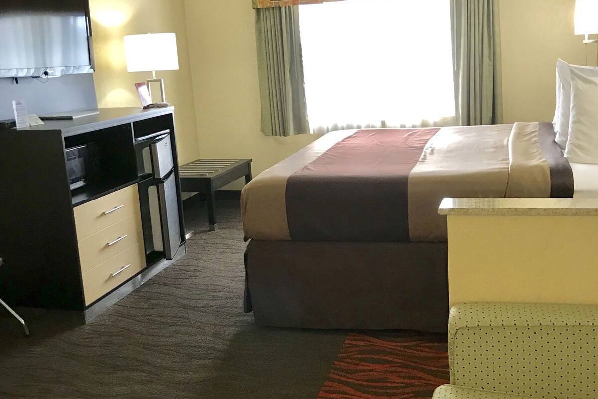 Quarto de hotel com cama, escrivaninha, televisão e uma cômoda.