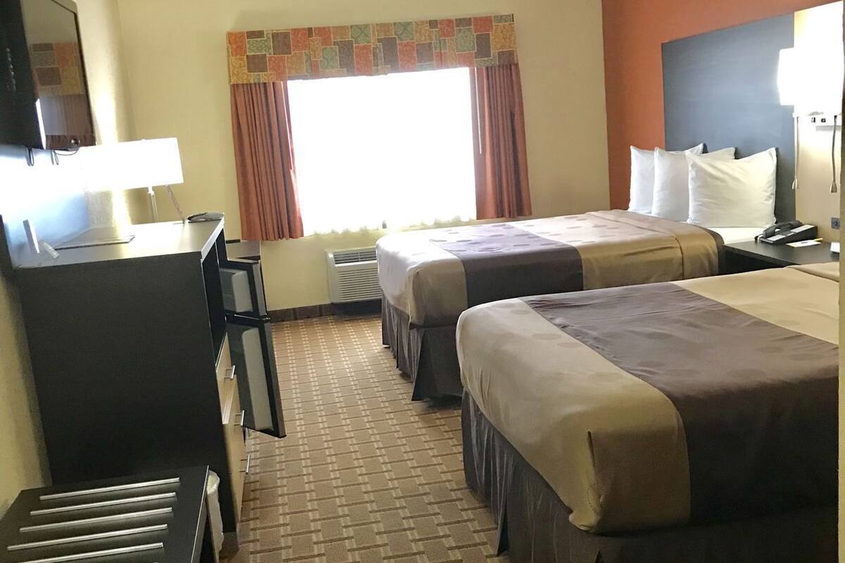 Quarto de hotel com duas camas, uma escrivaninha, uma cadeira, uma televisão e uma janela com cortinas.