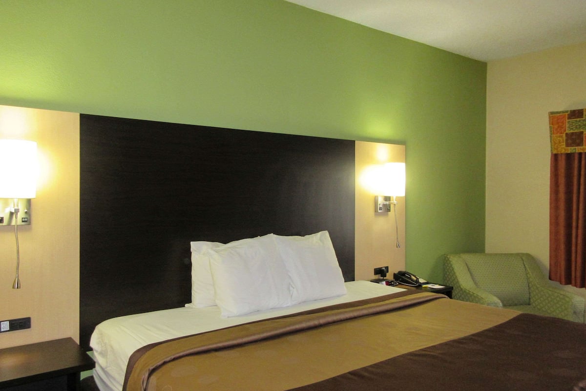 Quarto de hotel com uma cama grande, duas luminárias de cabeceira, uma poltrona verde e um telefone na mesa de apoio.