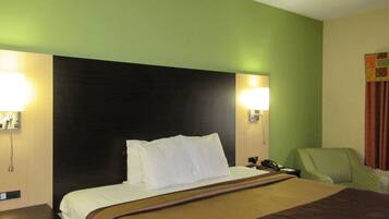 A hotel room with a large bed, two bedside lamps, a green armchair, and a telephone on the nightstand.