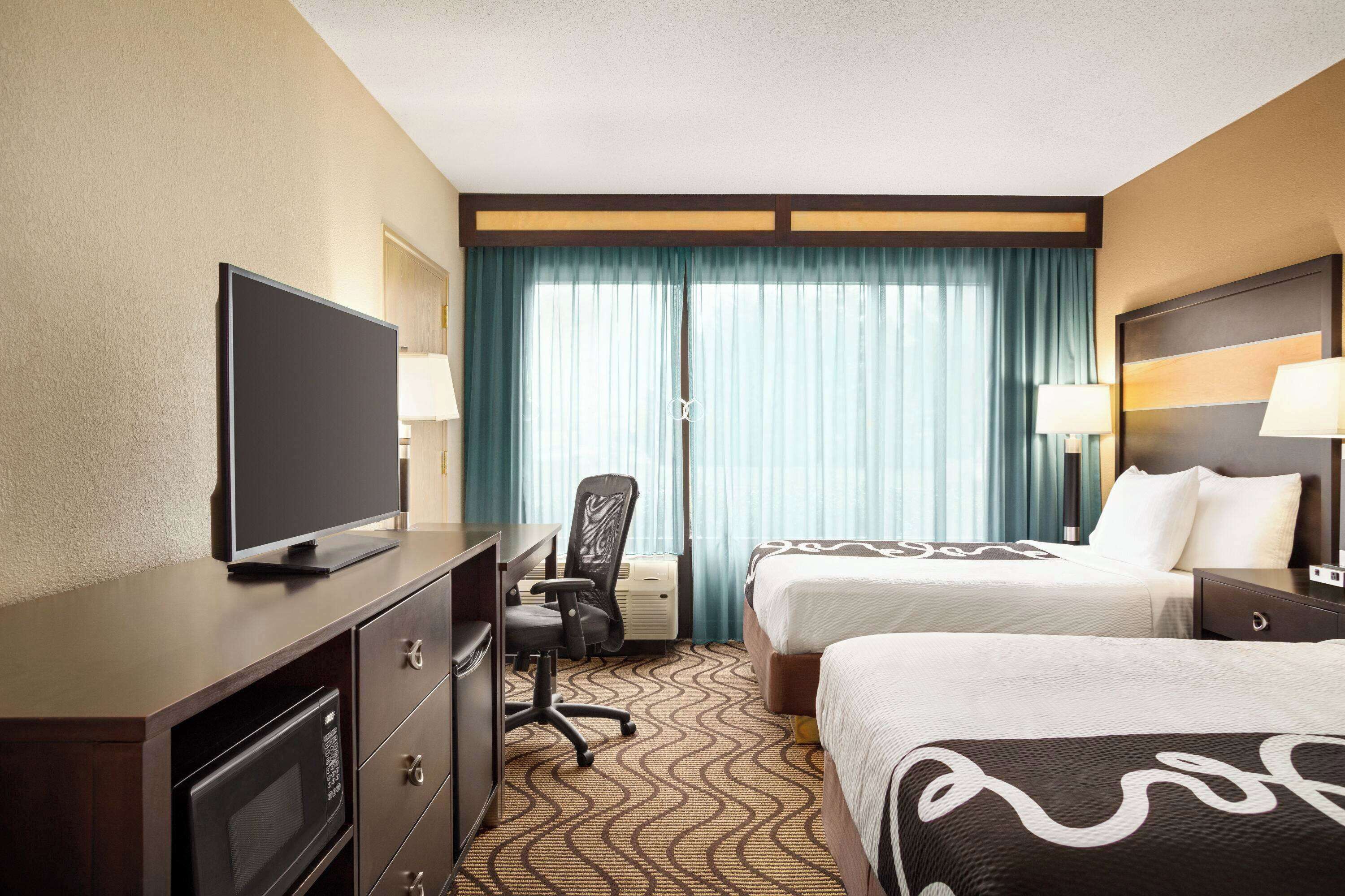 Une chambre d’hôtel avec deux lits, un bureau avec une télévision, une chaise et un four à micro-ondes.