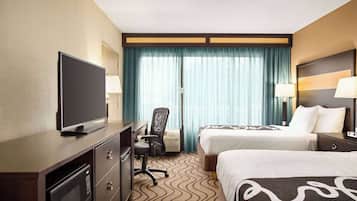 A hotel room with two beds, a desk with a television, a chair, and a microwave.