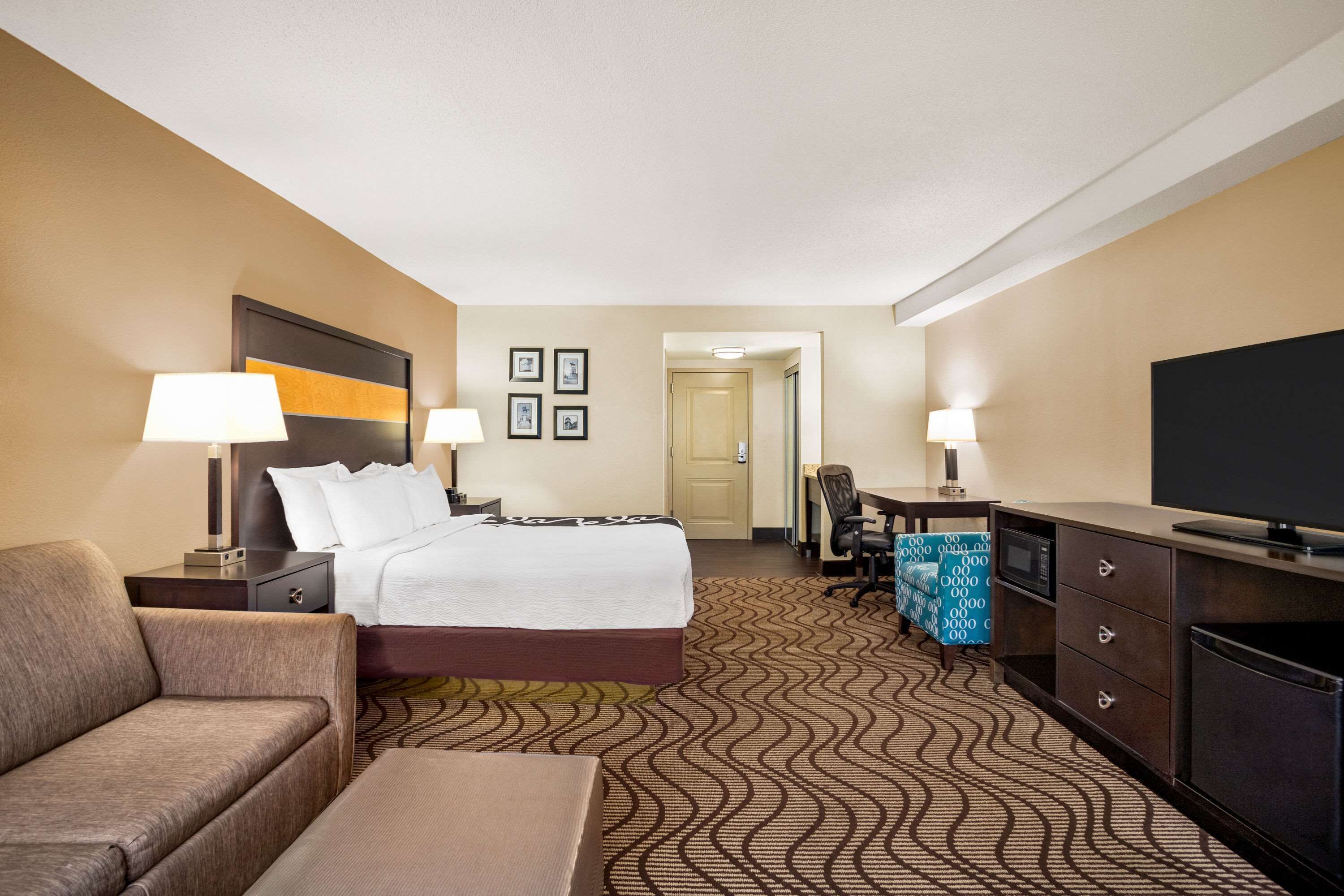A hotel room with a bed, two bedside tables with lamps, a desk with a chair, a television, and a microwave.