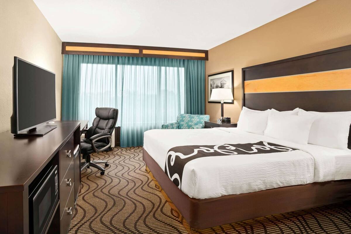 Hotelkamer met een bed, bureau met televisie, stoel, lamp en raam met gordijnen.