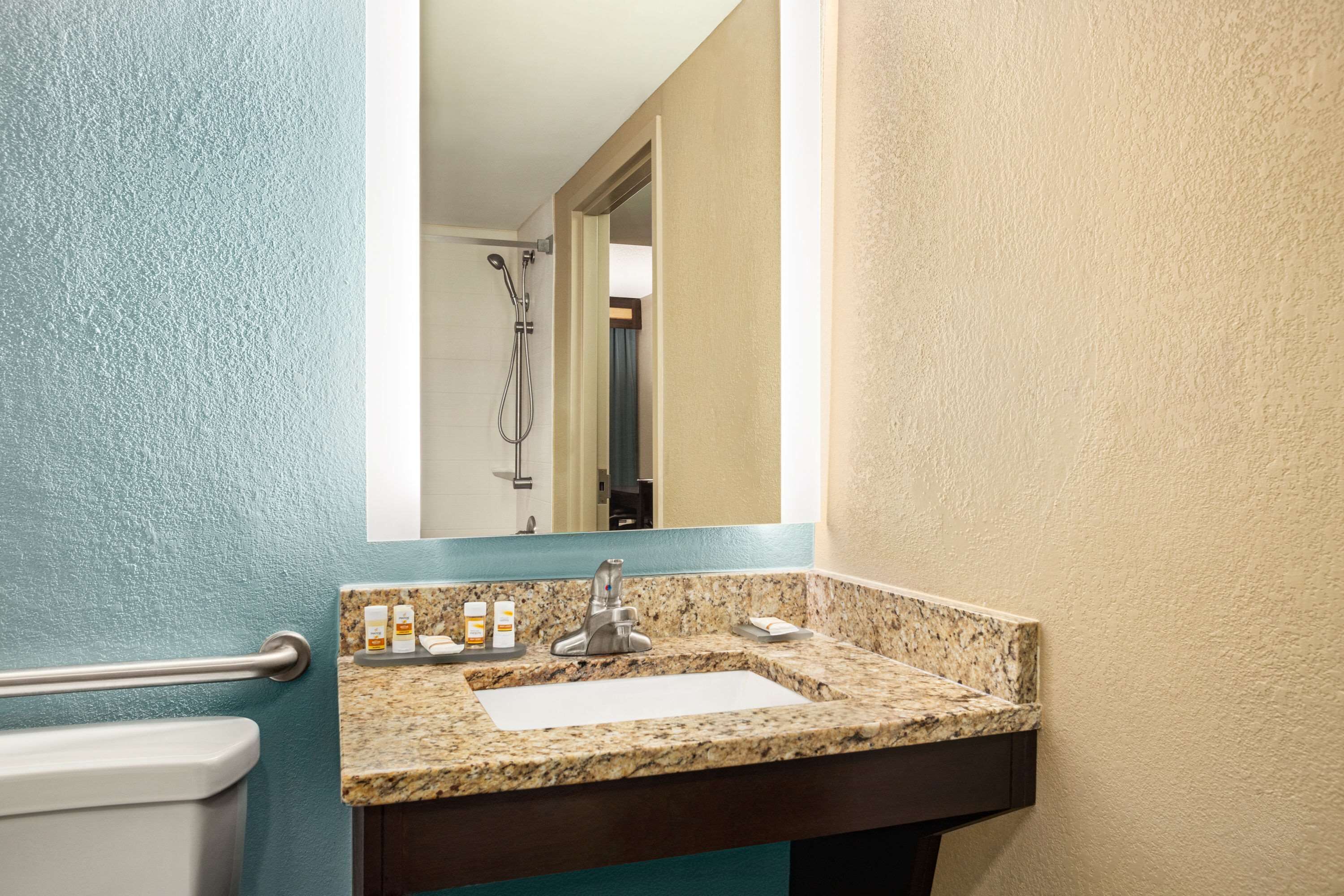 A bathroom with a granite countertop sink, a mirror, and a towel rack.