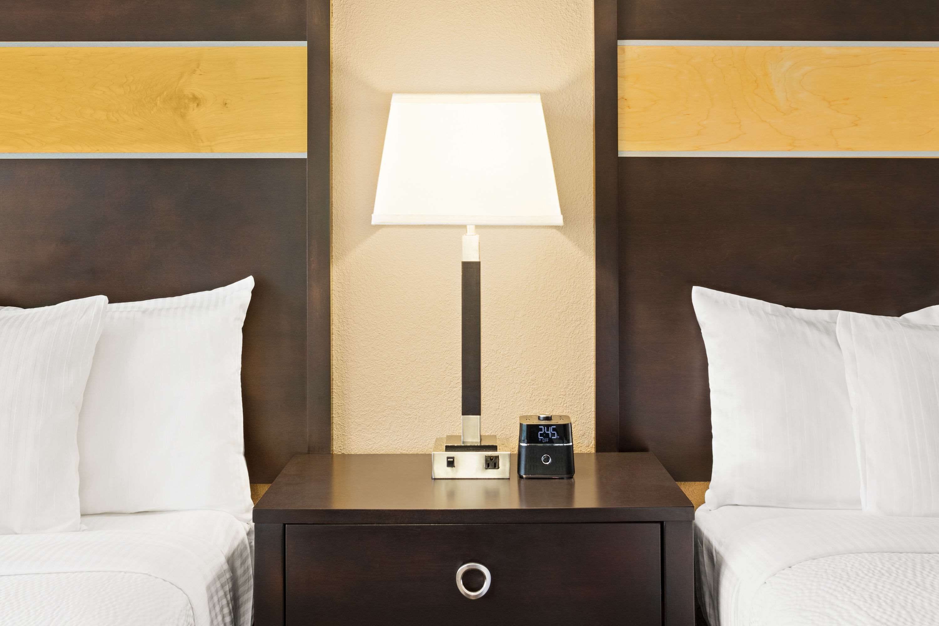 A hotel room with a bed, a nightstand with a lamp, and a digital clock.