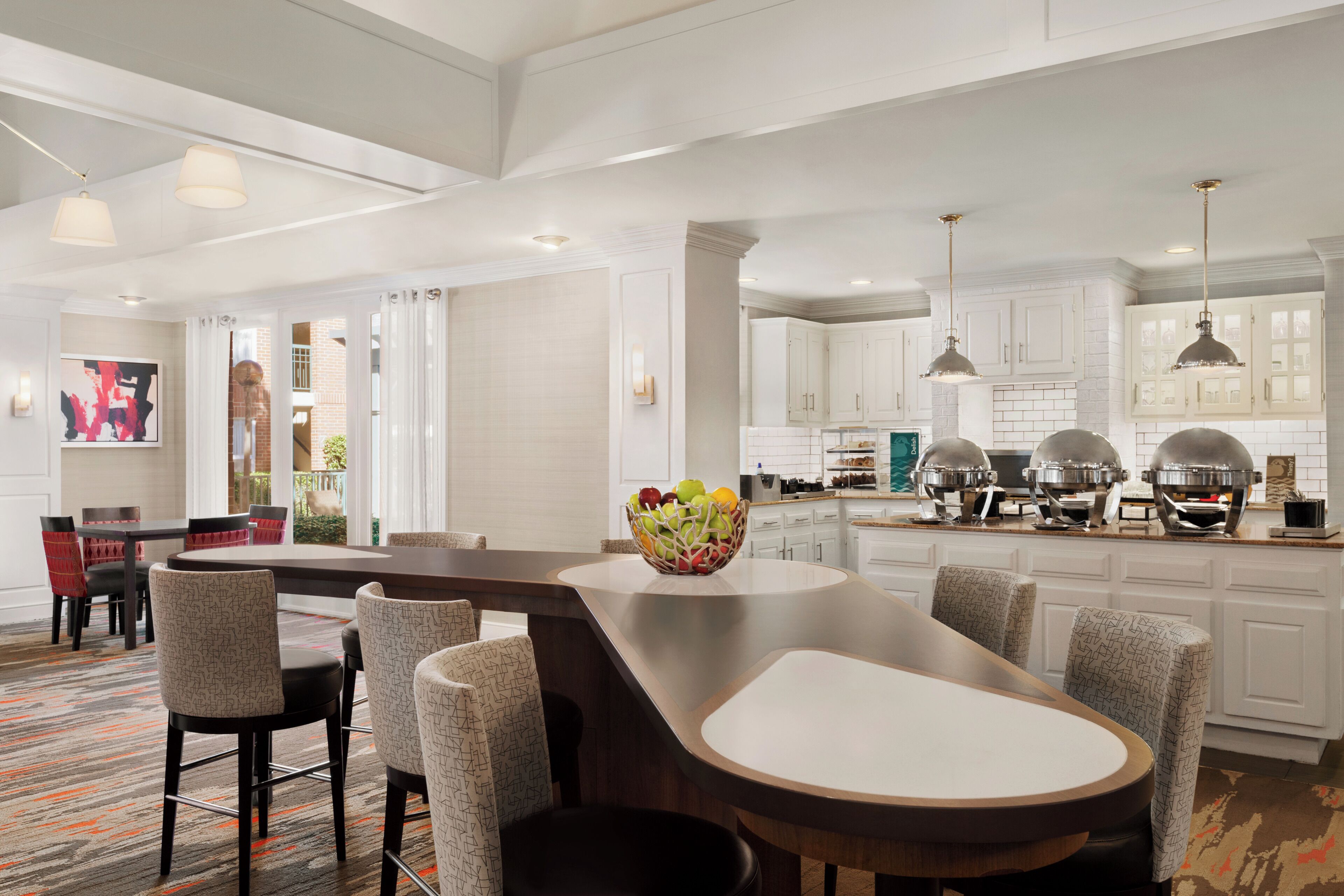 A modern kitchen with white cabinets, a central island with bar stools, and a dining area with a red chair.