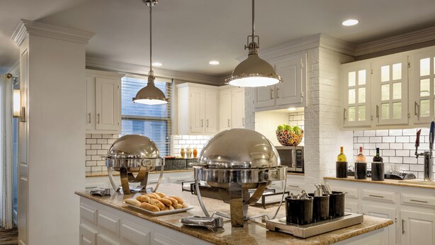 A spacious kitchen with white cabinetry, a large island with a built-in stove, and pendant lighting.