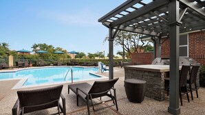 A poolside area with a barbecue station, lounge chairs, and umbrellas.