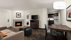 A modern living room with a fireplace, a television, a dining area, and a kitchen in the background.