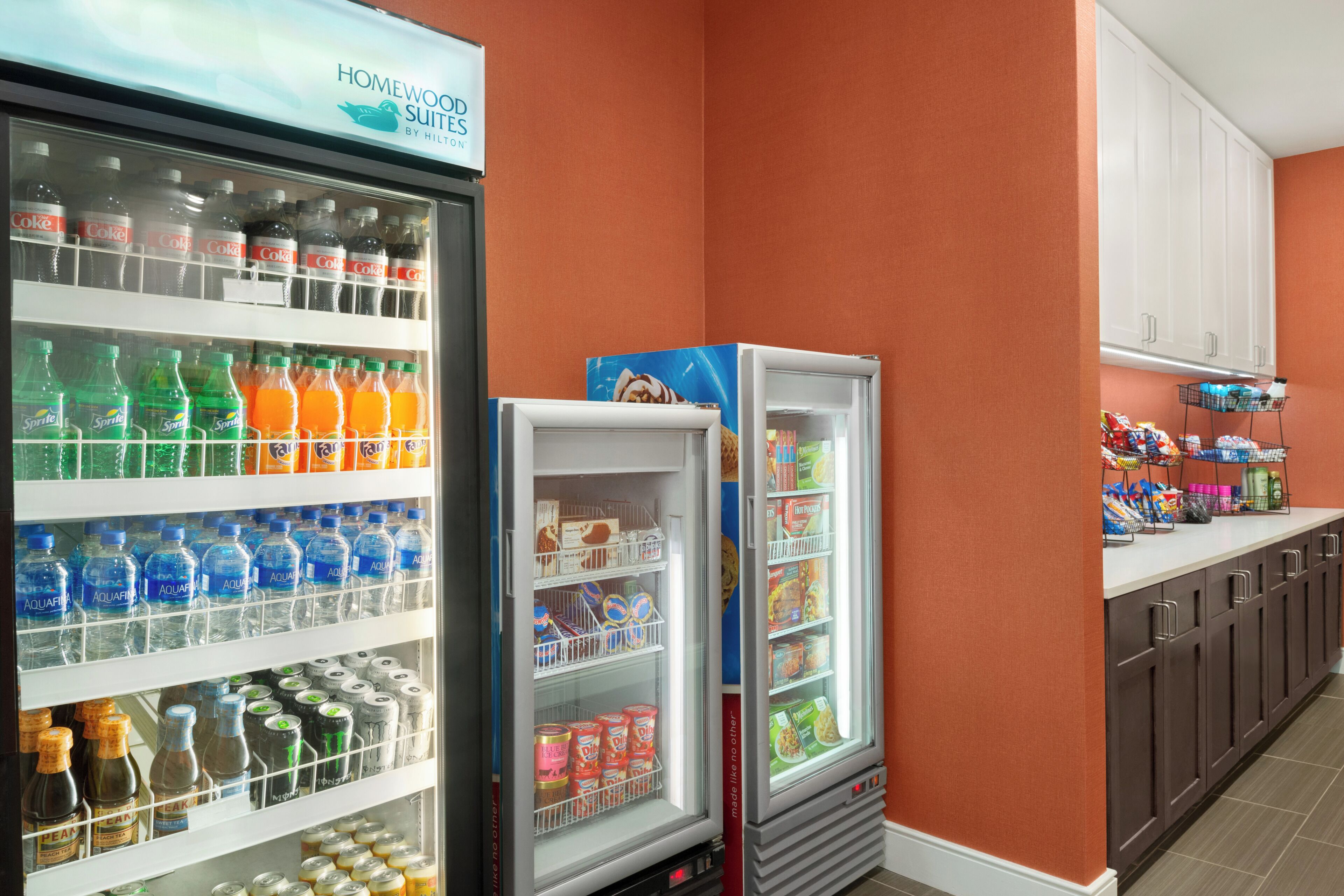 A hotel kitchenette with a refrigerator stocked with beverages and snacks, a microwave, and a sink.
