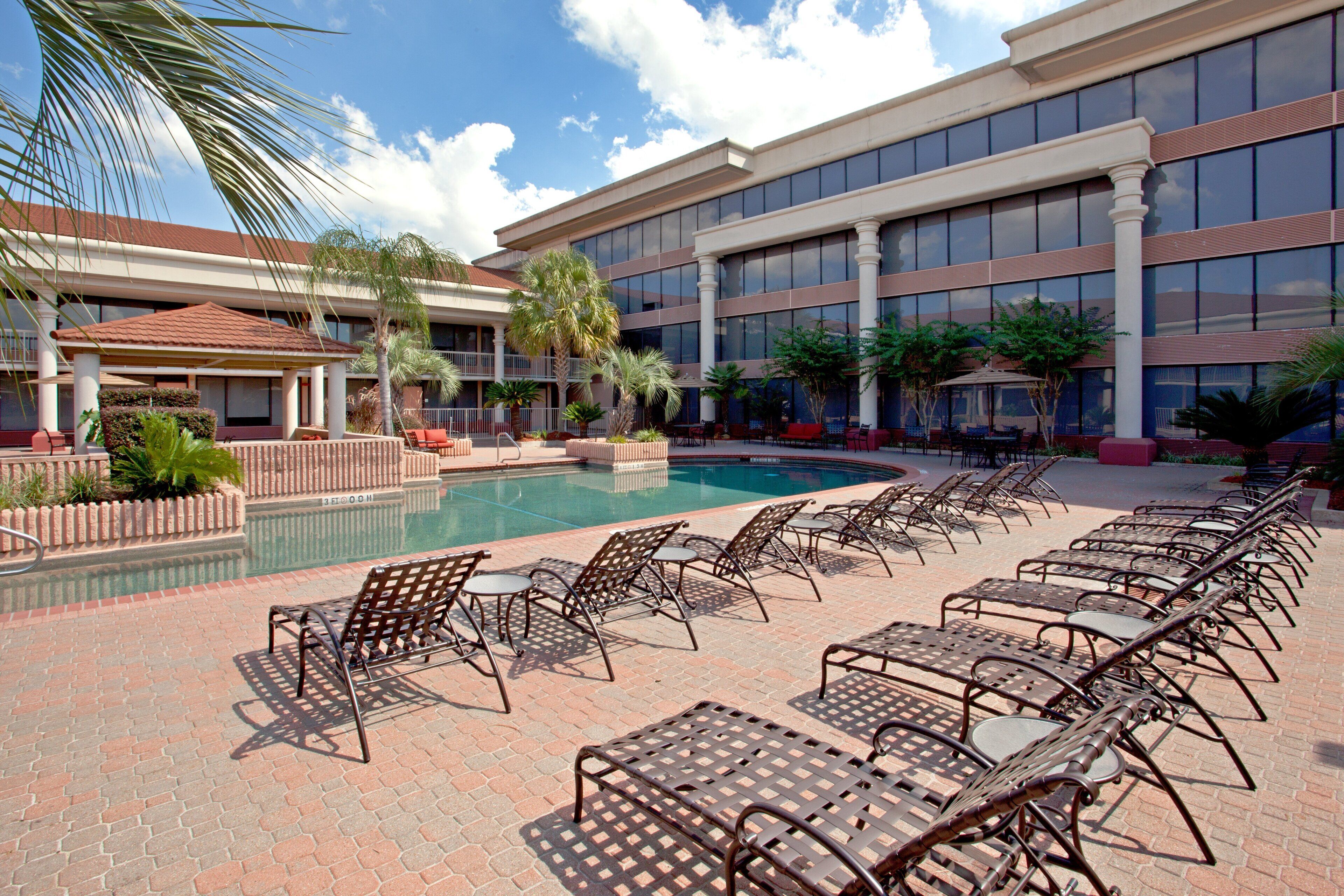 A pool area with lounge chairs and a building with large windows in the background.