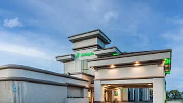 A modern building with a prominent 'Holiday Inn' sign, a parking area, and a gated entrance.