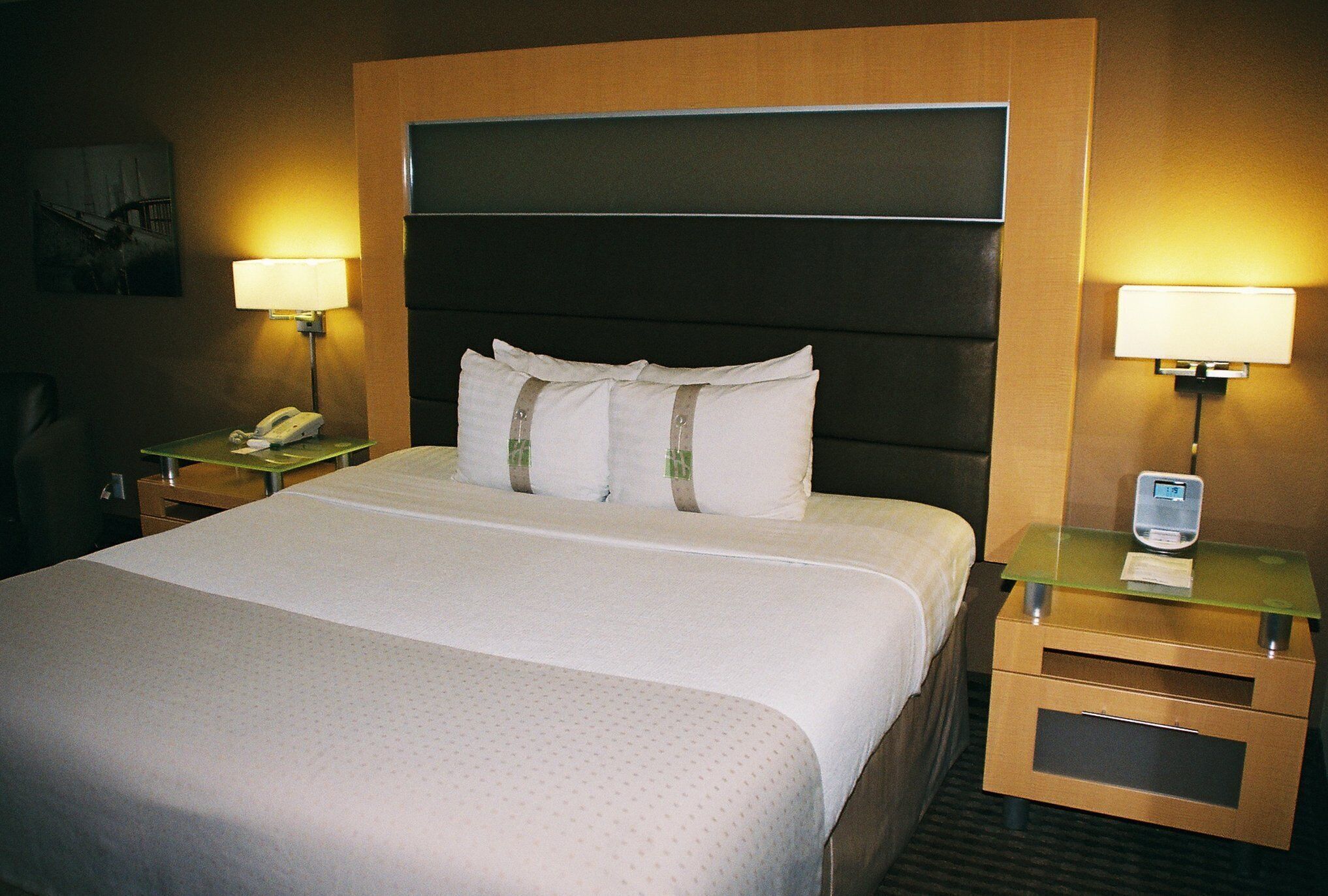 A hotel room with a large bed, two bedside tables, a nightstand, a lamp, and a digital clock.