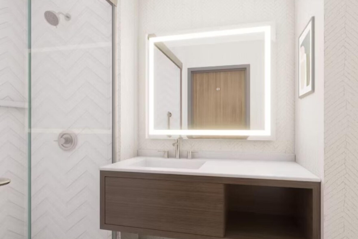 A bathroom with a glass shower enclosure, a white sink with a wooden vanity, and a mirror with a light.