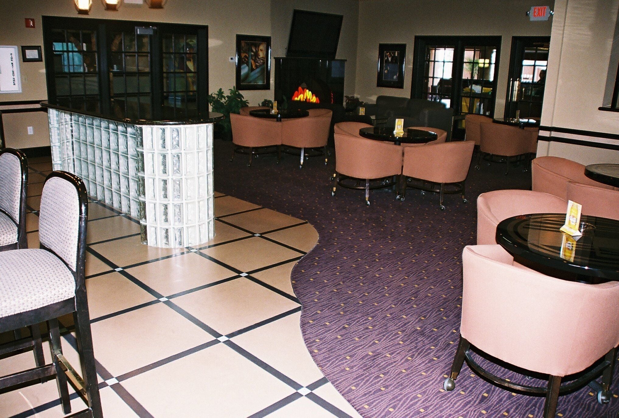Un hall d’entrée avec un sol à carreaux, un espace détente avec des chaises et des tables, une cheminée et un coin bar.