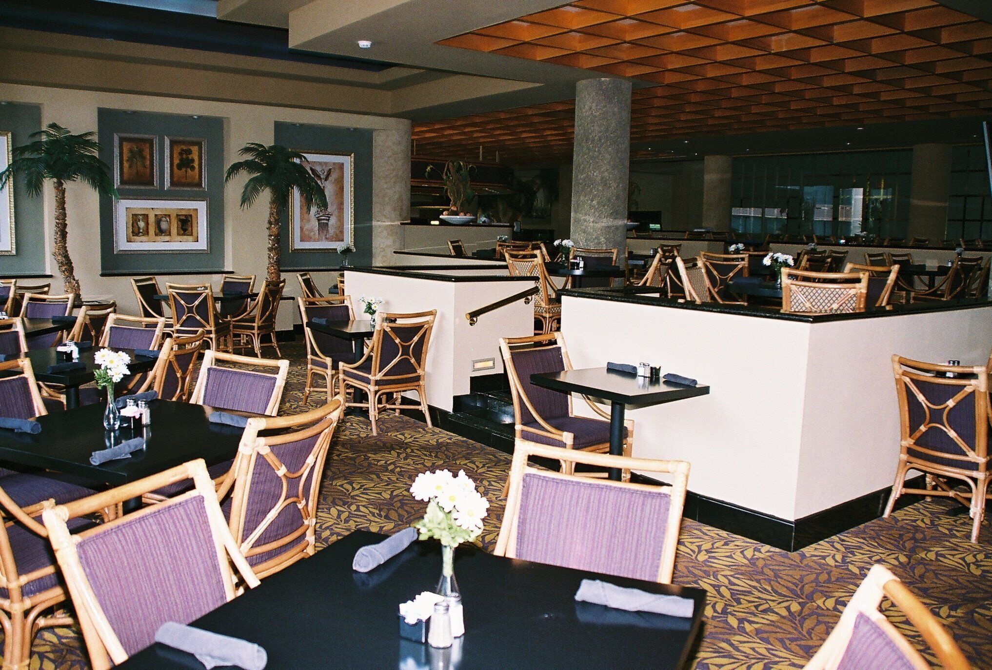 A hotel lobby with dining tables, wicker chairs, and a reception desk.