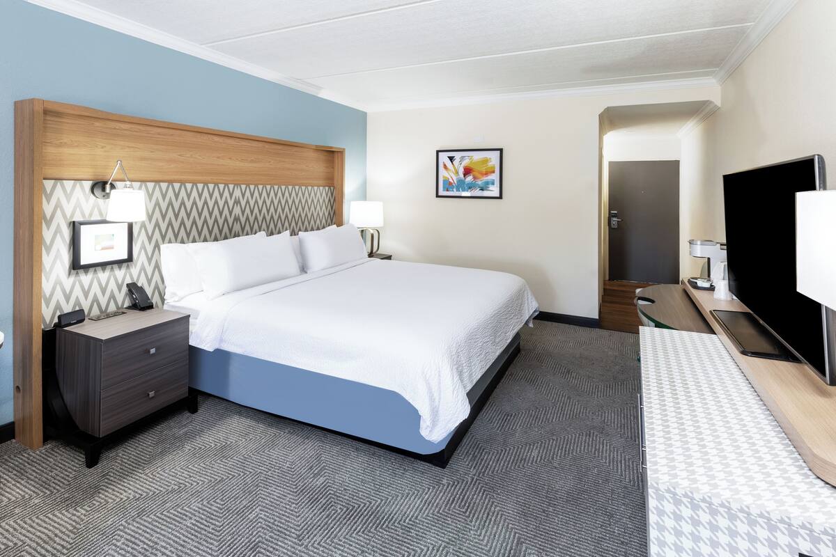 A hotel room with a bed, bedside tables, a TV, and a door.
