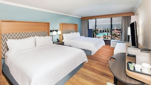 Habitación de hotel con dos camas, un escritorio con cafetera, televisión y vista a una piscina y zona exterior.